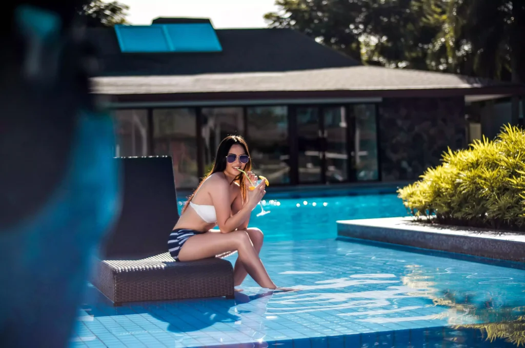 Jeune femme sirotant un cocktail, assise sur un transat dans une piscine avec plage immergée