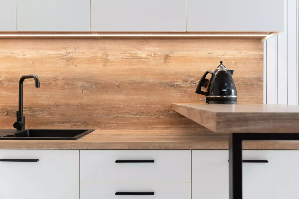 vue sur un plan de travail stratifié effet bois dans un cuisine blanche et épurée, avec un évier noir et une bouilloire noire
